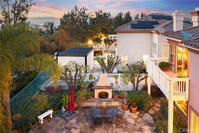 patio terrace at dusk with an outdoor fireplace and a storage shed