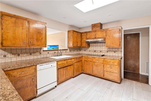 kitchen with a skylight, dishwasher, sink, backsplash, and light hardwood / wood-style floors