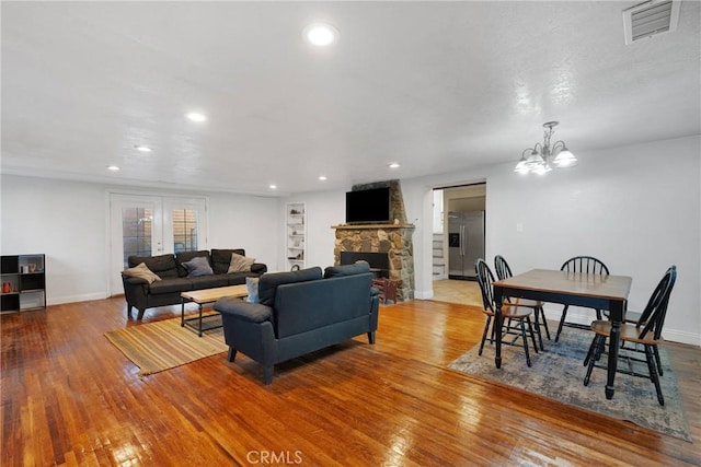 living room with french doors, a stone fireplace, a chandelier, and light hardwood / wood-style flooring