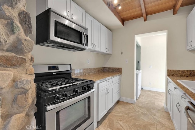 kitchen with appliances with stainless steel finishes, beamed ceiling, white cabinetry, wood ceiling, and light stone countertops