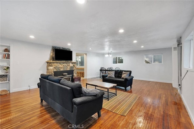 living room featuring wood-type flooring, a stone fireplace, and a notable chandelier