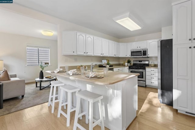 kitchen featuring sink, white cabinetry, light hardwood / wood-style flooring, appliances with stainless steel finishes, and a kitchen breakfast bar