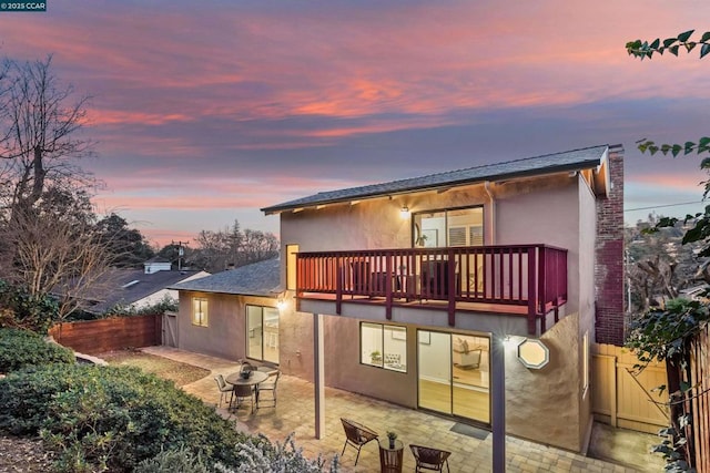 back house at dusk featuring a balcony and a patio