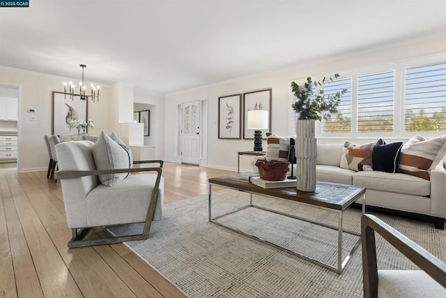 living room with an inviting chandelier, ornamental molding, and light hardwood / wood-style floors