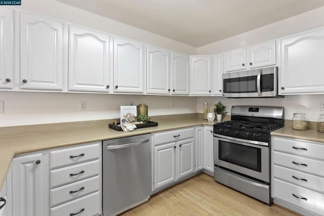 kitchen with stainless steel appliances, white cabinetry, and light hardwood / wood-style flooring