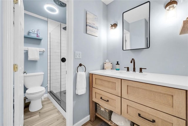 bathroom with baseboards, toilet, wood finished floors, vanity, and a shower stall