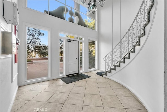 tiled foyer entrance with stairs, a high ceiling, baseboards, and a notable chandelier