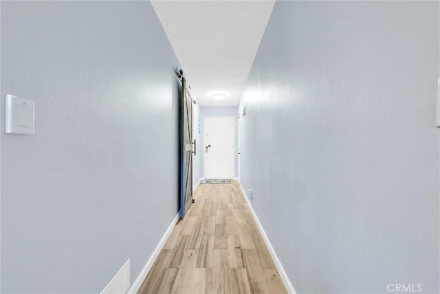 hallway with light wood-style floors, baseboards, and a barn door