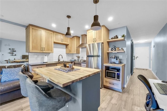 kitchen featuring stainless steel appliances, tasteful backsplash, wooden counters, light brown cabinetry, and wall chimney range hood