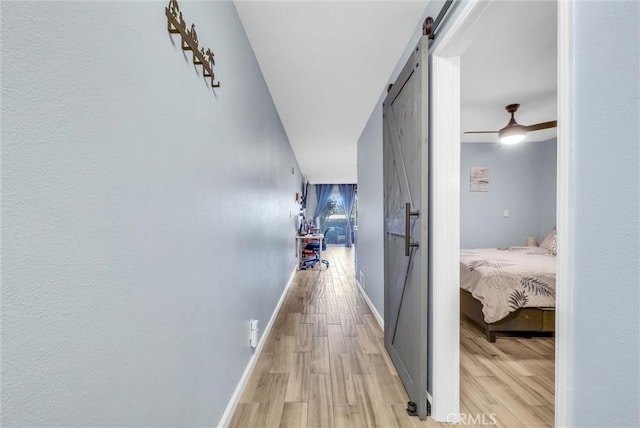 hall with a barn door, light wood-style flooring, and baseboards