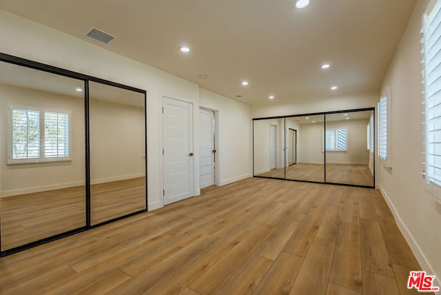 unfurnished bedroom with two closets and light wood-type flooring