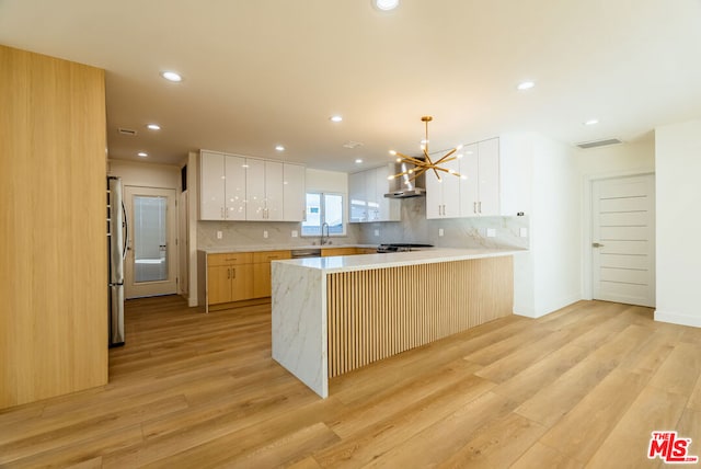 kitchen with wall chimney range hood, white cabinetry, hanging light fixtures, stainless steel appliances, and kitchen peninsula