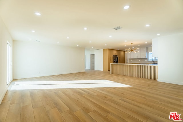 unfurnished living room featuring an inviting chandelier and light wood-type flooring