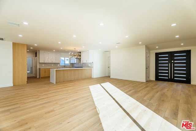 kitchen featuring pendant lighting, white cabinets, a chandelier, light hardwood / wood-style floors, and a spacious island