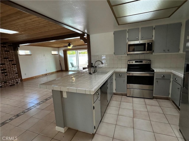 kitchen with stainless steel appliances, tile counters, kitchen peninsula, and gray cabinets