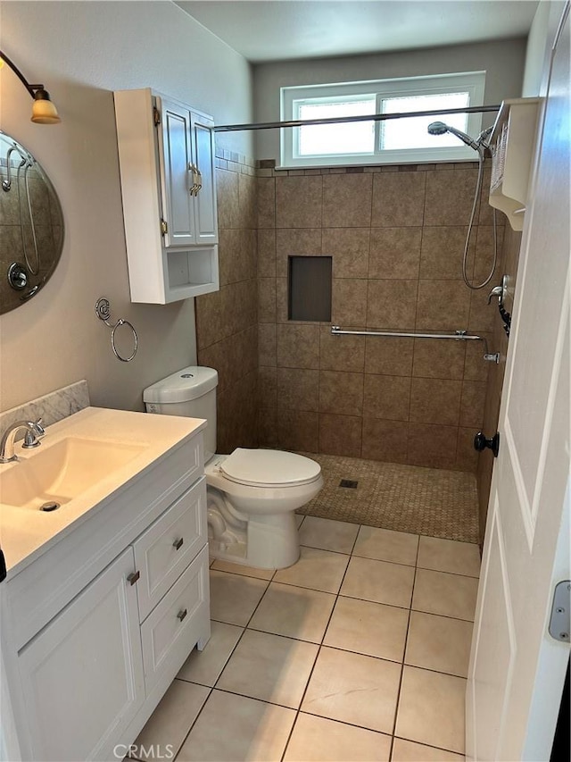 bathroom with tile patterned flooring, vanity, a tile shower, and toilet