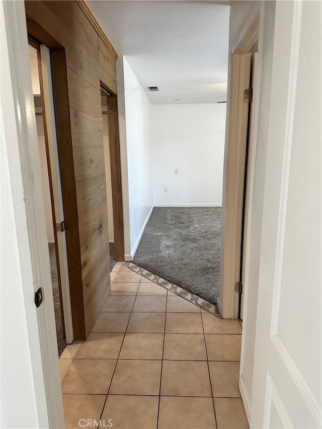 hallway featuring wooden walls and light tile patterned flooring