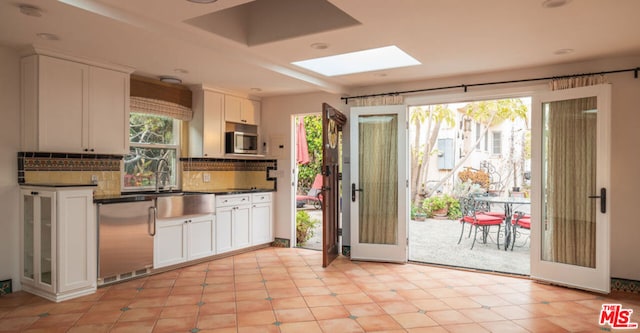 kitchen with sink, white cabinetry, a skylight, refrigerator, and backsplash