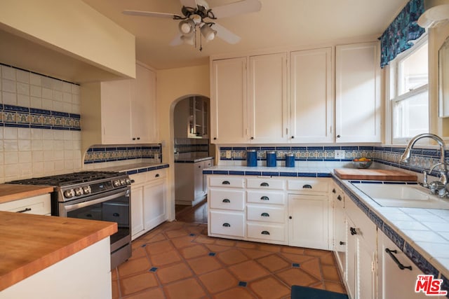 kitchen with sink, butcher block countertops, white cabinetry, stainless steel gas range oven, and decorative backsplash