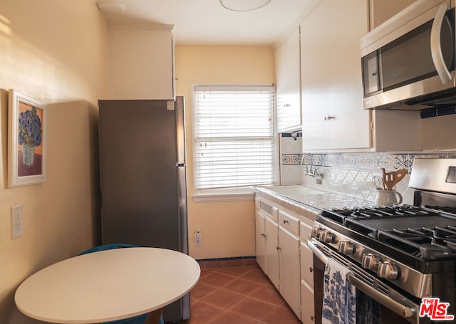 kitchen with white cabinetry, appliances with stainless steel finishes, dark tile patterned floors, and backsplash