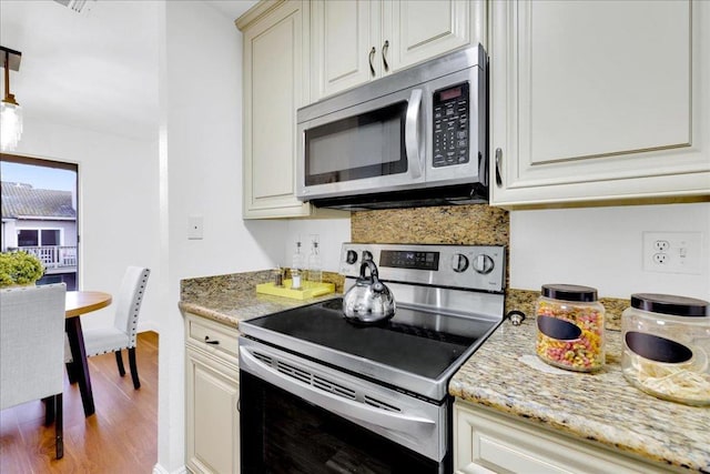 kitchen with stainless steel appliances, tasteful backsplash, cream cabinets, light stone counters, and light hardwood / wood-style floors