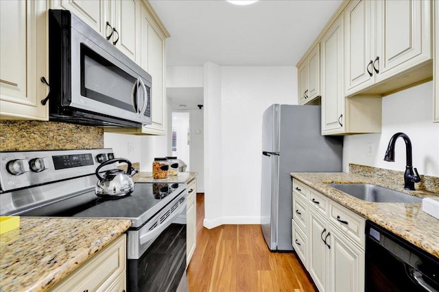 kitchen featuring appliances with stainless steel finishes, sink, light stone counters, and light hardwood / wood-style floors