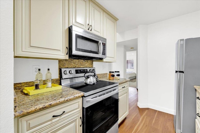 kitchen featuring light stone countertops, stainless steel appliances, cream cabinetry, and light wood-type flooring