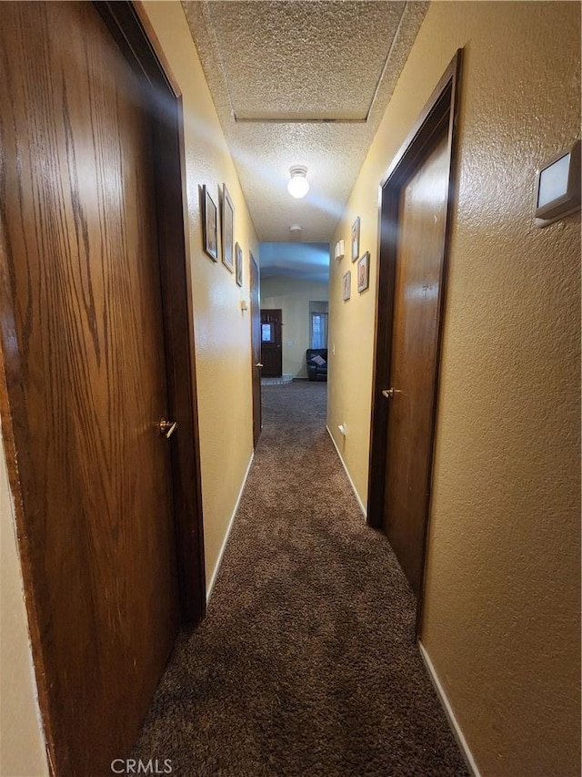 hall featuring a textured ceiling and dark colored carpet