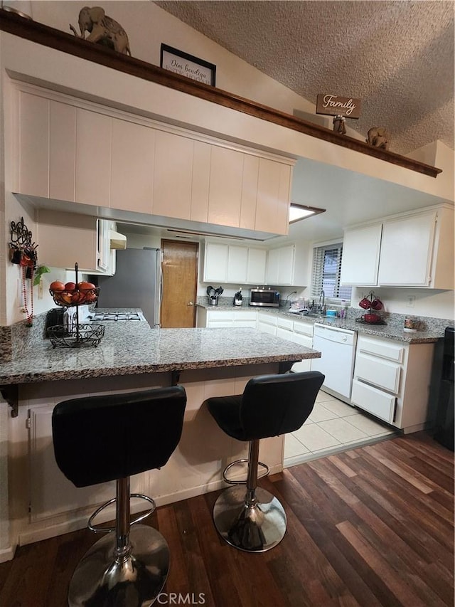 kitchen featuring white cabinetry, light stone countertops, dishwasher, and kitchen peninsula