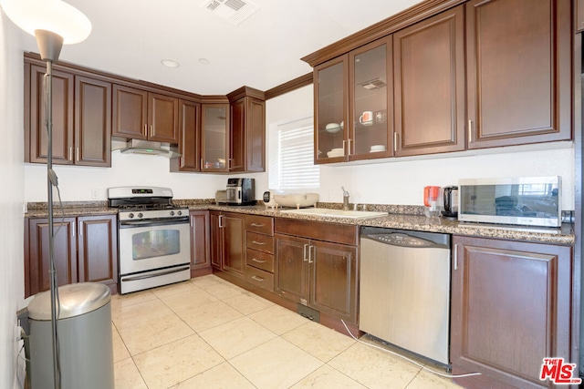 kitchen with sink, light tile patterned floors, appliances with stainless steel finishes, ornamental molding, and dark stone counters