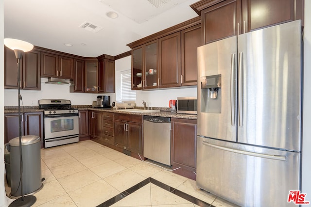 kitchen featuring sink, light tile patterned floors, dark brown cabinets, stainless steel appliances, and dark stone counters