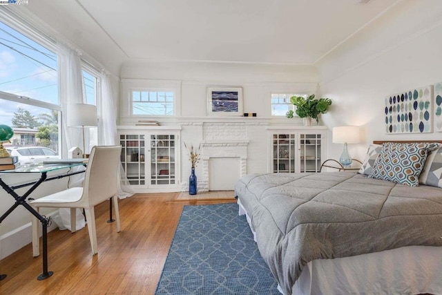 bedroom featuring multiple windows, wood-type flooring, and a fireplace