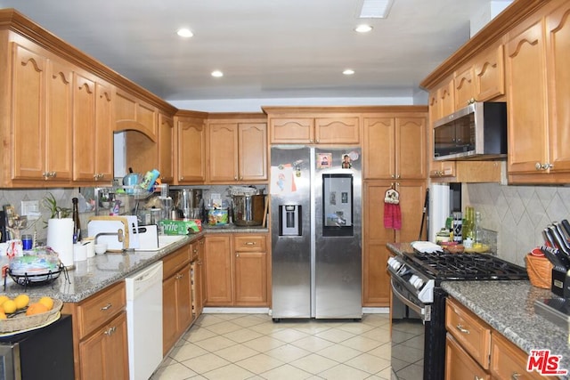 kitchen featuring light tile patterned flooring, appliances with stainless steel finishes, decorative backsplash, and dark stone counters