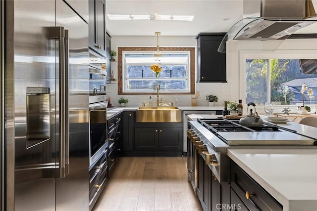 kitchen featuring sink, high end refrigerator, hanging light fixtures, light hardwood / wood-style flooring, and range hood