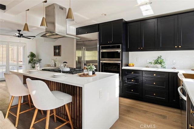 kitchen with a kitchen island, stainless steel appliances, island exhaust hood, a kitchen bar, and decorative light fixtures