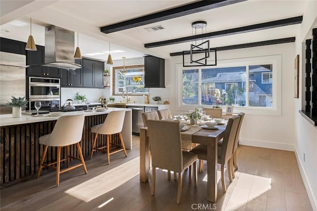 dining room featuring beamed ceiling, sink, an inviting chandelier, and light wood-type flooring