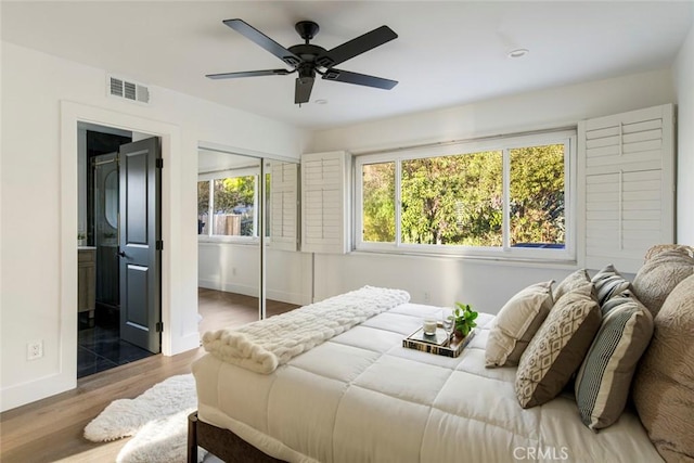 bedroom with multiple windows, ensuite bathroom, dark hardwood / wood-style floors, and ceiling fan