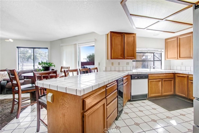 kitchen featuring tile counters, white dishwasher, kitchen peninsula, and a wealth of natural light