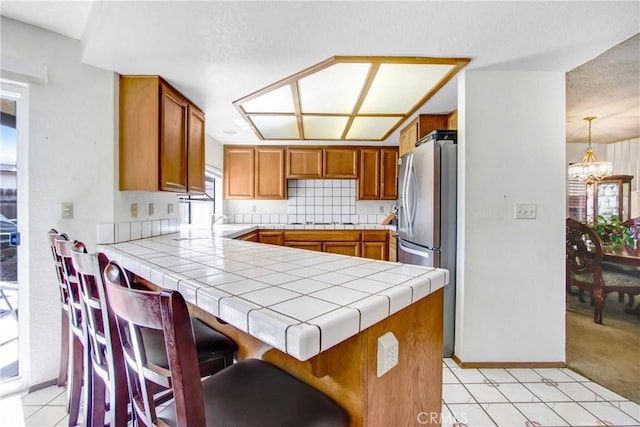 kitchen featuring pendant lighting, a breakfast bar, tile countertops, kitchen peninsula, and a chandelier