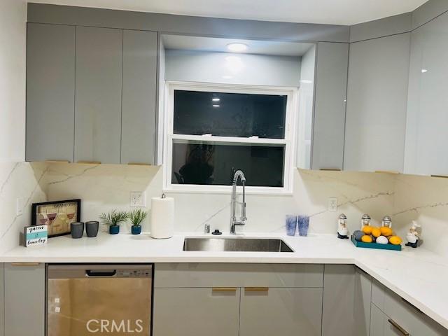 kitchen featuring gray cabinets, dishwasher, sink, and tasteful backsplash