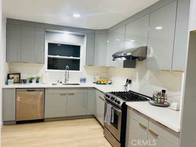 kitchen with sink, light hardwood / wood-style flooring, gray cabinets, appliances with stainless steel finishes, and extractor fan