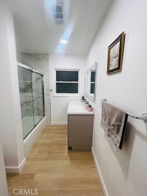 bathroom featuring wood-type flooring, vanity, and shower / bath combination with glass door