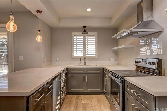 kitchen with a raised ceiling, hanging light fixtures, exhaust hood, kitchen peninsula, and stainless steel appliances