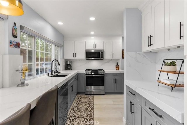 kitchen with sink, gray cabinetry, light stone counters, appliances with stainless steel finishes, and decorative backsplash