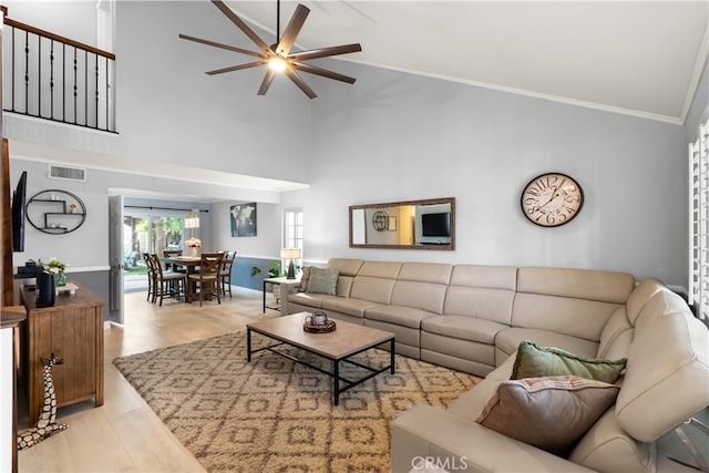 living room with crown molding, light wood-type flooring, ceiling fan, and a high ceiling