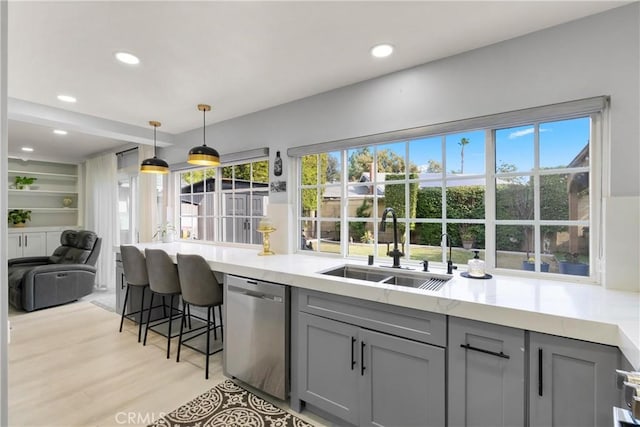 kitchen featuring sink, decorative light fixtures, light hardwood / wood-style flooring, stainless steel dishwasher, and gray cabinets