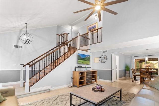 living room featuring a towering ceiling, ceiling fan with notable chandelier, and light wood-type flooring