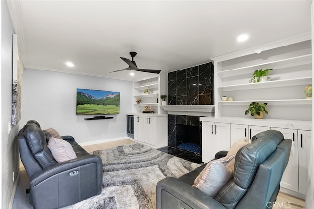 living room with built in shelves, crown molding, light hardwood / wood-style flooring, ceiling fan, and a premium fireplace