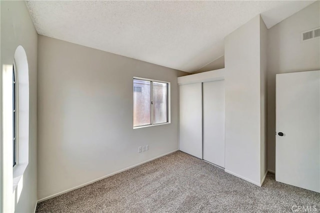 unfurnished bedroom with lofted ceiling, light colored carpet, a closet, and a textured ceiling