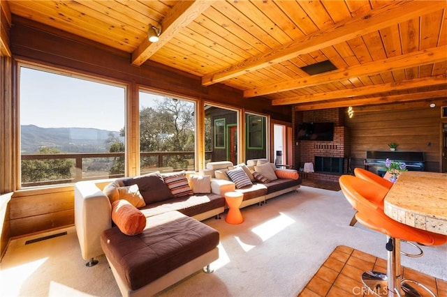 sunroom with a mountain view, a brick fireplace, wooden ceiling, and beam ceiling